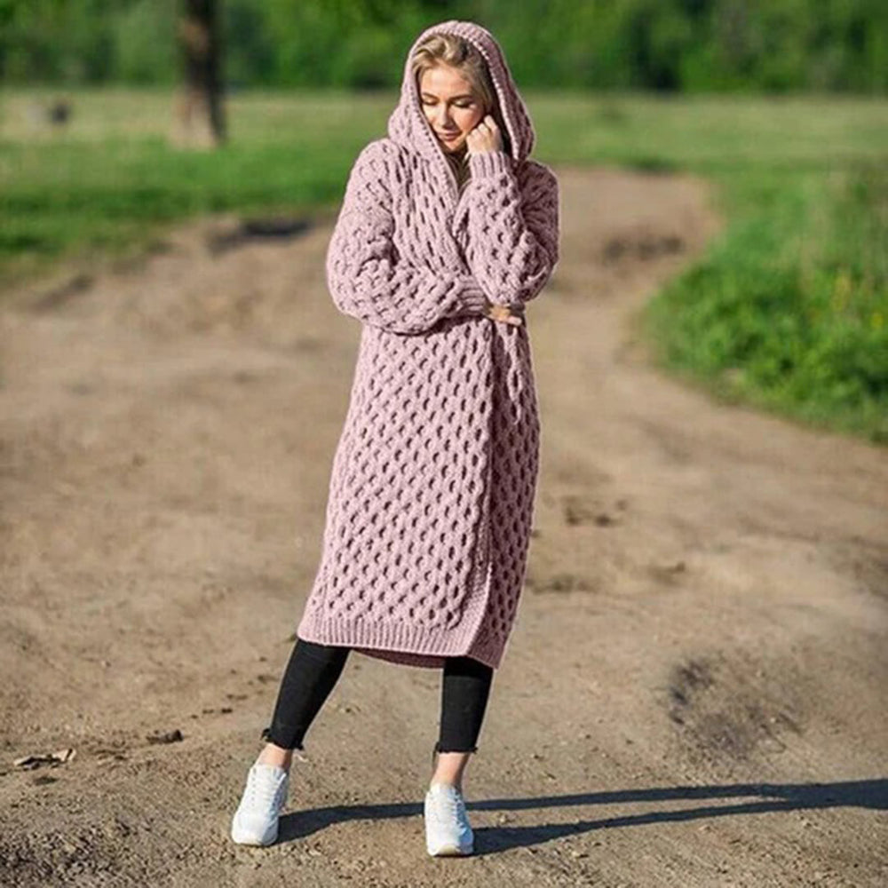 Frau in rosa Strickmantel mit Kapuze steht auf einem Feldweg. Modetrend, Strickmode, Herbstoutfit, gemütlicher Look, Damenmode.