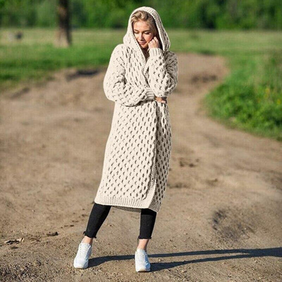 Frau in beigem Strickmantel mit Kapuze steht auf einem Feldweg. Modetrend, Strickmode, Herbstoutfit, gemütlicher Look, Damenbekleidung.