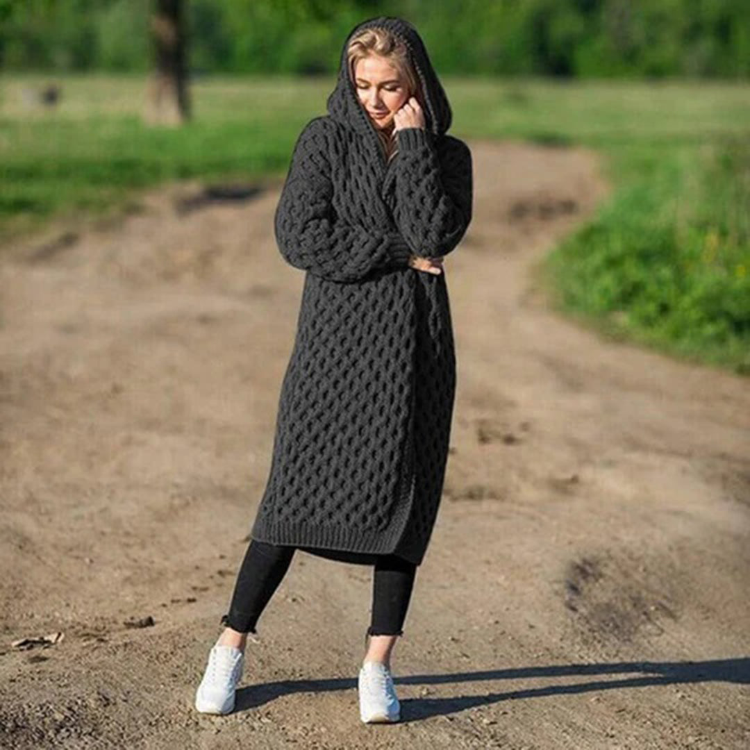 Frau in grauem Strickmantel mit Kapuze steht auf einem Feldweg. Modetrend, Strickmode, Herbstoutfit, gemütlicher Look, Damenbekleidung.