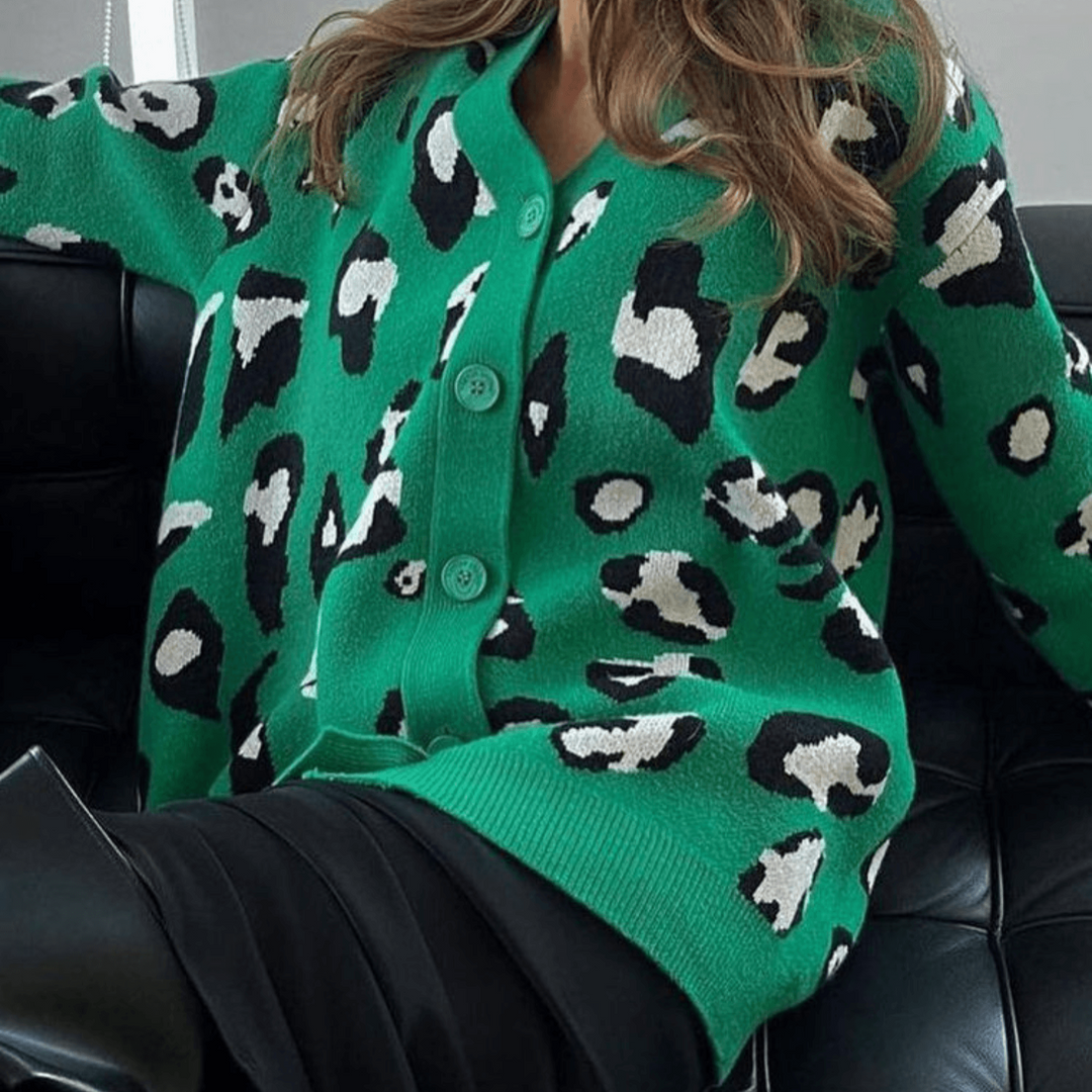 Grüner Cardigan mit schwarz-weißem Leopardenmuster, getragen von einer Person auf einem schwarzen Ledersofa. Modetrend, Damenmode, Strickjacke.
