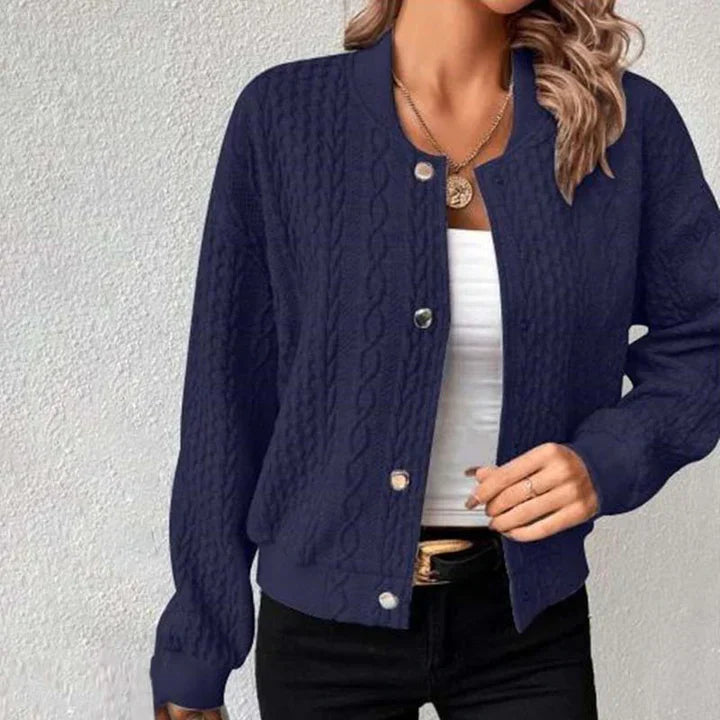Frau trägt dunkelblaue Strickjacke mit Zopfmuster, weißes Top und schwarze Hose. Modische Damenbekleidung, lässiger Stil, Herbstmode.