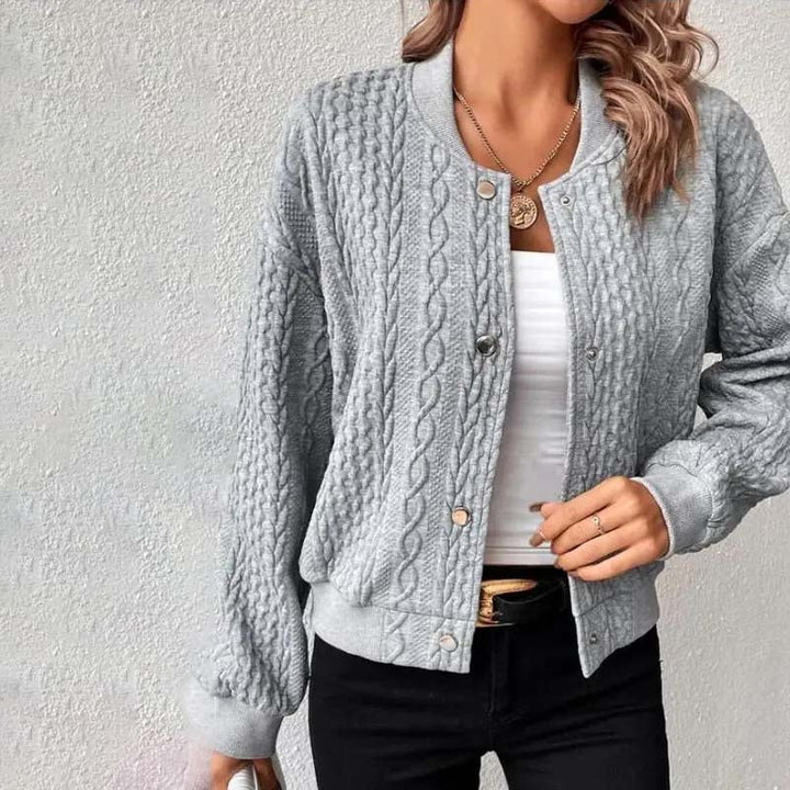 Frau trägt graue Strickjacke mit Zopfmuster, weißes Top und schwarze Hose. Modetrend, Damenmode, lässiger Stil, Herbstoutfit.