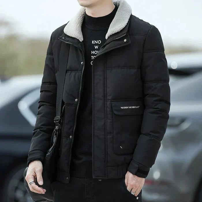 Mann in schwarzer Winterjacke mit Fellkragen, modisch und warm, steht draußen. Perfekte Herrenbekleidung für kalte Jahreszeiten.