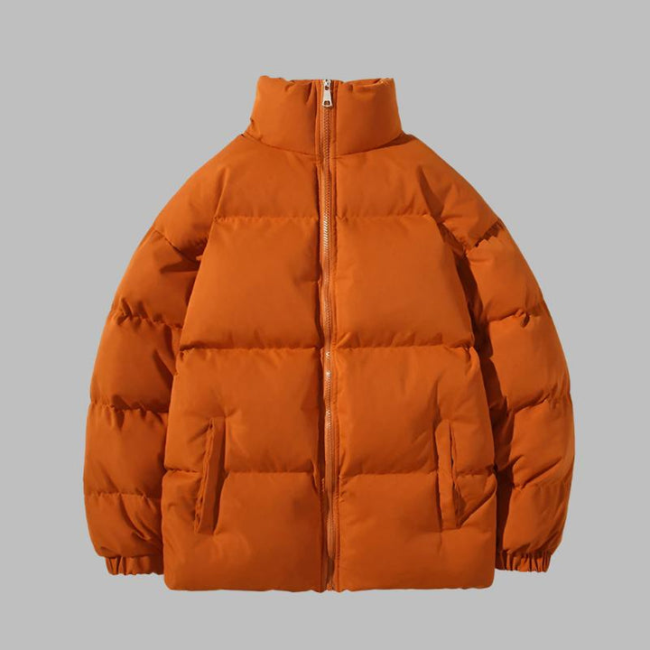 Orangefarbene Daunenjacke mit Reißverschluss, Stehkragen und Seitentaschen vor grauem Hintergrund. Wintermode, warme Outdoor-Bekleidung.