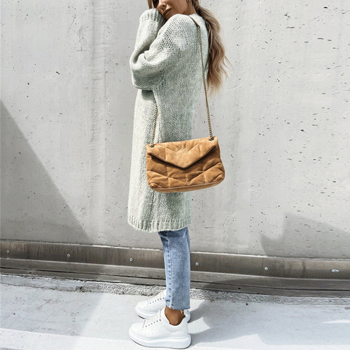 Frau in grauem Strickpullover, blauer Jeans und weißen Sneakers, trägt braune Umhängetasche. Modetrend Herbst, lässiger Streetstyle Look.