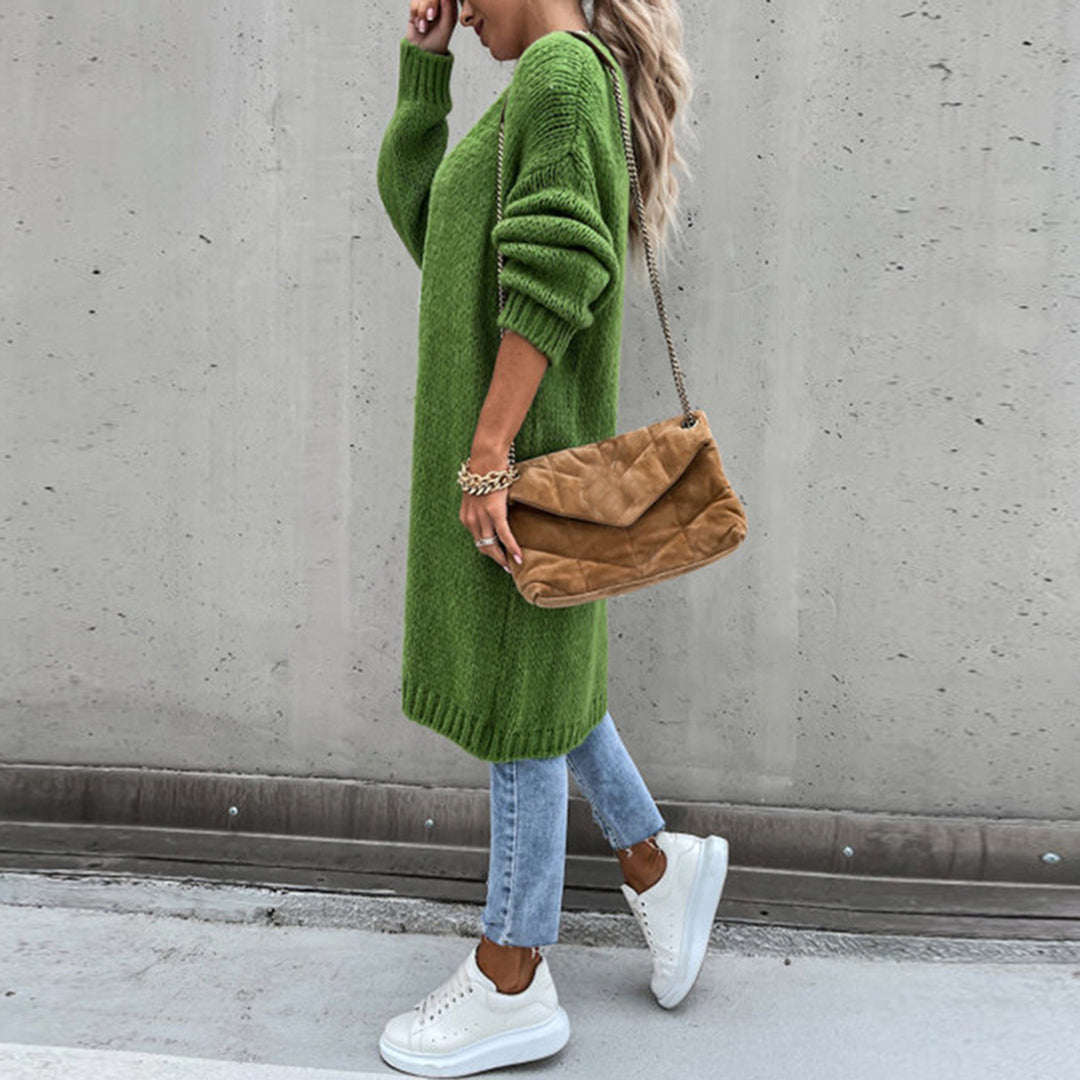 Frau in grünem Strickkleid, blauer Jeans und weißen Sneakers, trägt braune Umhängetasche. Streetstyle Mode, lässiger Herbstlook.