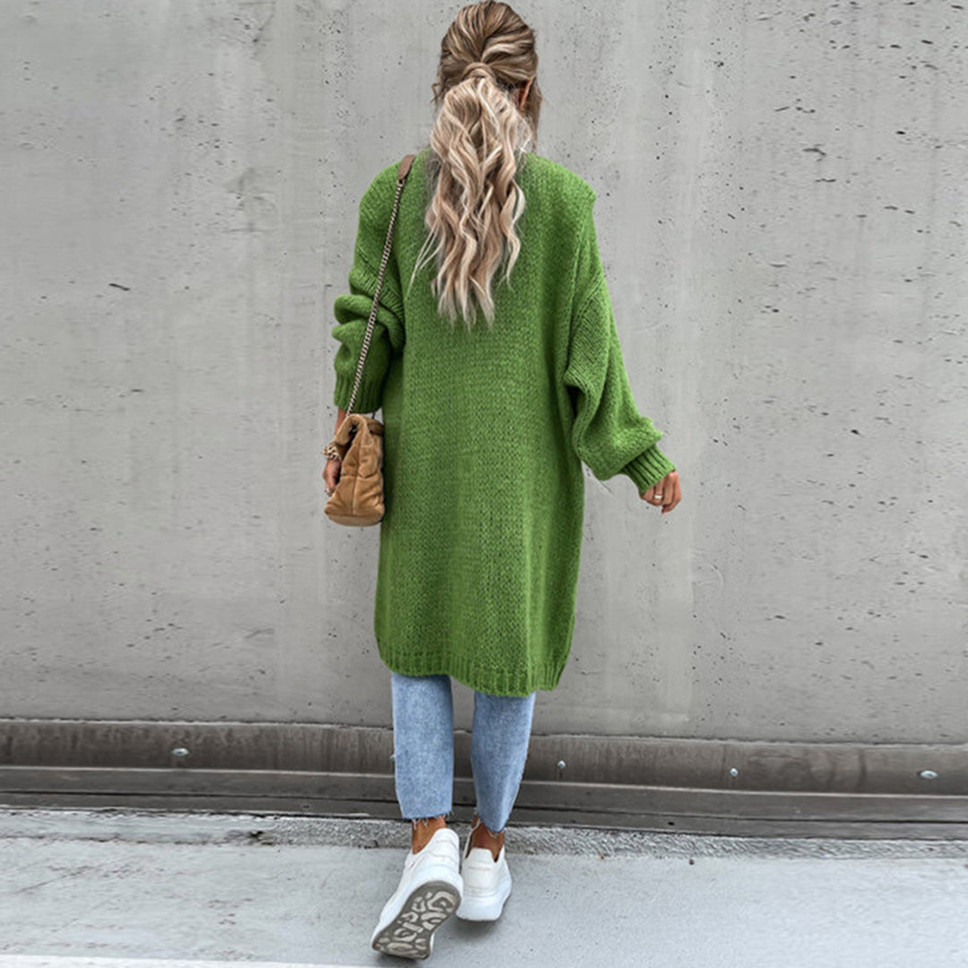 Frau mit grünem Strickpullover, blauer Jeans und weißen Sneakers vor Betonwand. Lässiger Herbstlook, modische Damenbekleidung, Streetstyle.
