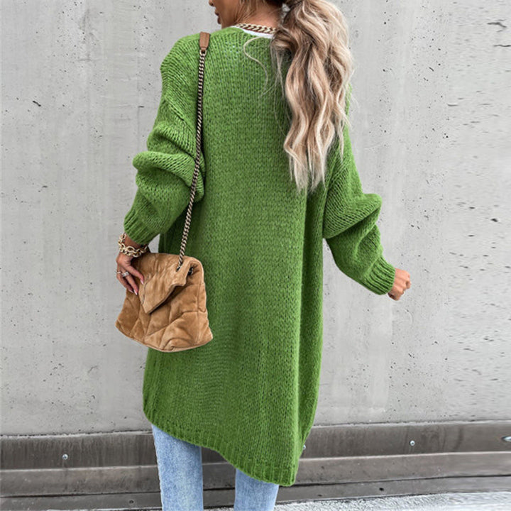 Frau in grünem Strickpullover und blauer Jeans, trägt braune Handtasche. Modetrend Herbst, lässiger Streetstyle, Betonwand Hintergrund.