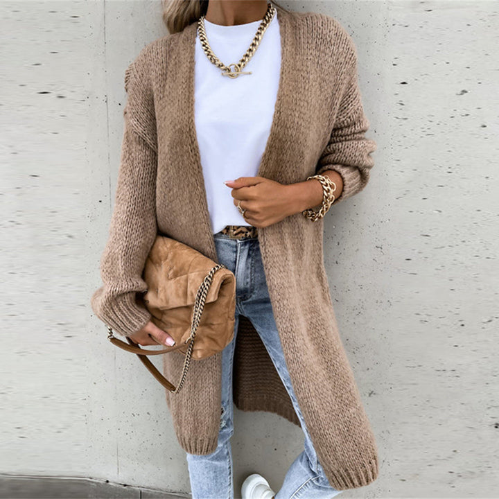 Frau in beigem Strickcardigan, weißem T-Shirt und blauer Jeans, hält braune Handtasche. Modetrend Herbst, lässiger Streetstyle Look.