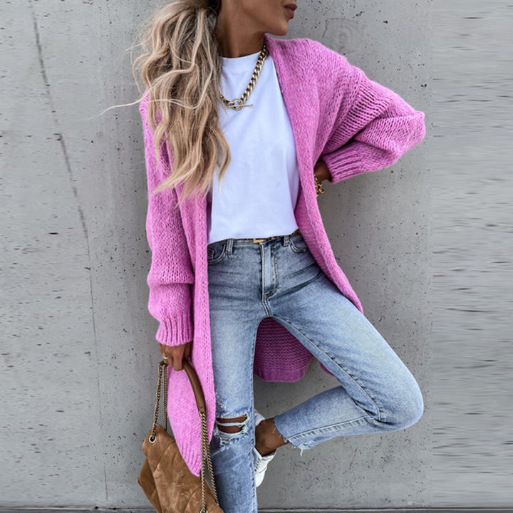 Frau in rosa Strickjacke, weißem T-Shirt und zerrissenen Jeans vor grauer Wand. Modetrend, lässiger Stil, Herbstmode, Streetwear.