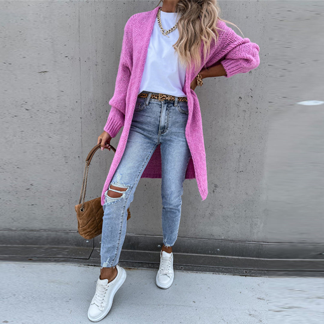 Frau in rosa Strickjacke, weißem T-Shirt, zerrissenen Jeans und weißen Sneakers vor grauer Wand. Modetrend, lässiger Streetstyle, Herbstmode.
