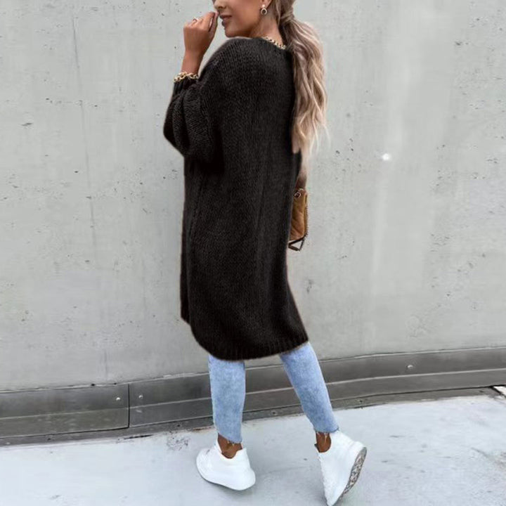 Frau in schwarzem Strickpullover, blauer Jeans und weißen Sneakers vor grauer Wand. Modetrend, lässiger Herbstlook, Streetstyle.