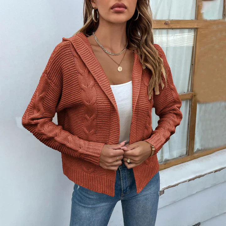 Frau trägt orange Strickjacke mit Zopfmuster, weißes Top und Jeans. Modetrend Herbst, lässiger Stil, Damenmode, gemütlicher Look.
