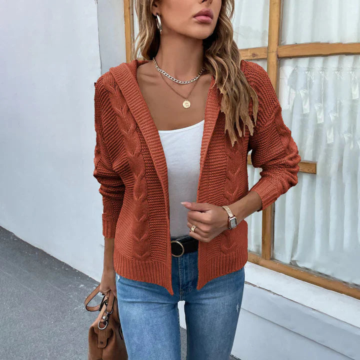 Frau in orangefarbener Strickjacke, weißem Top und blauer Jeans vor einem Fenster. Modetrend, Herbstmode, lässiger Stil, Damenbekleidung.