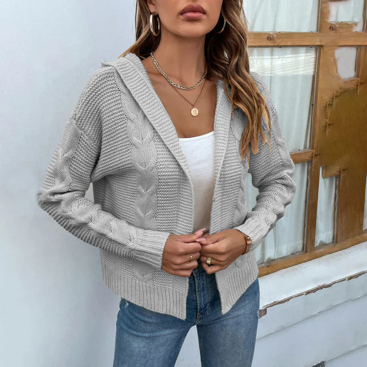 Frau trägt grauen Strick-Cardigan mit Zopfmuster, weißes Top und Jeans. Modetrend Herbst, lässiger Stil, Damenmode, gemütlicher Look.