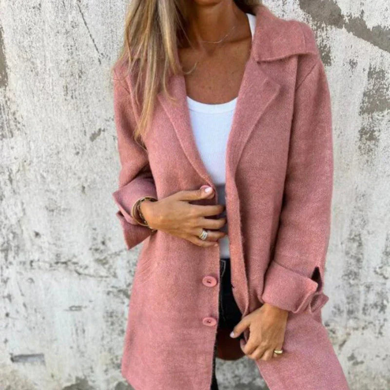 Frau in rosa Mantel vor Betonwand, trägt weißes Top und Jeans. Modetrend Herbst, stilvolle Damenbekleidung, lässiger Look.