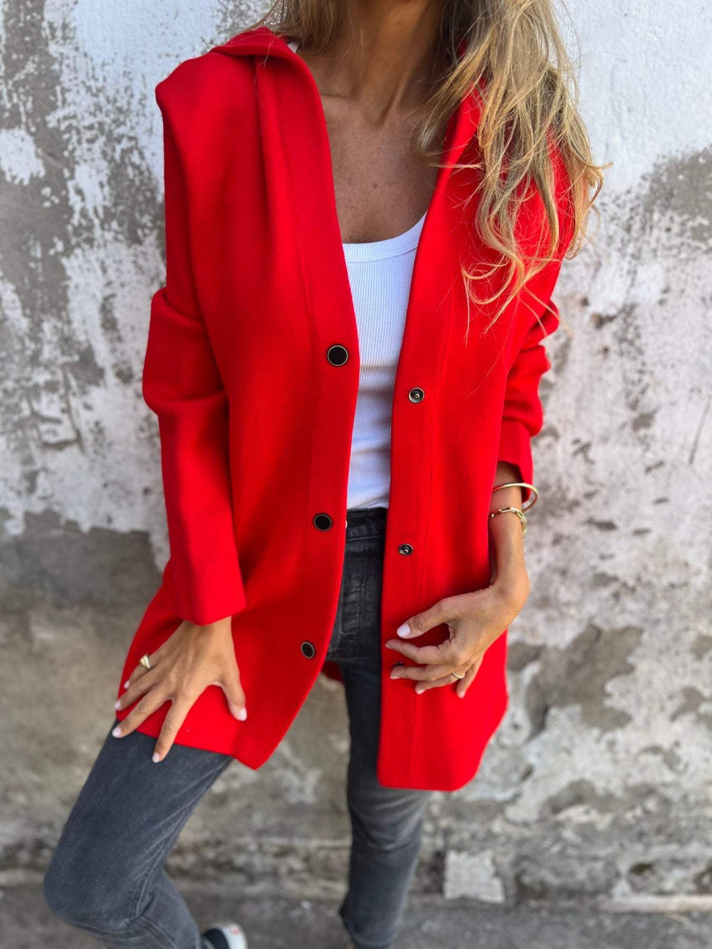 Frau in rotem Mantel und weißem Top vor einer Betonwand. Modetrend, Herbstmode, stilvolle Damenbekleidung, lässiger Look.