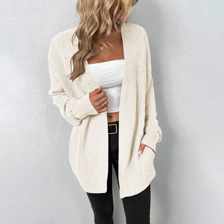 Blonde Frau in weißem Strick-Cardigan, weißem Top und schwarzer Hose vor grauem Hintergrund. Modetrend, Damenmode, lässiger Look.
