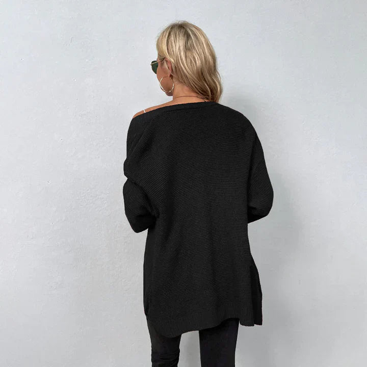 Frau mit blonden Haaren trägt schwarzen Oversize-Pullover und Sonnenbrille, steht vor grauer Wand. Modetrend, lässiger Look, Herbstmode.