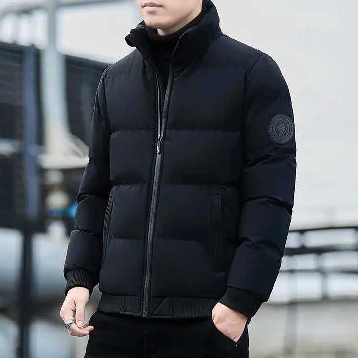 Mann in schwarzer Daunenjacke, Reißverschluss geschlossen, urbaner Hintergrund. Wintermode, warme Jacke, stilvoll, modern, Outdoor-Bekleidung.