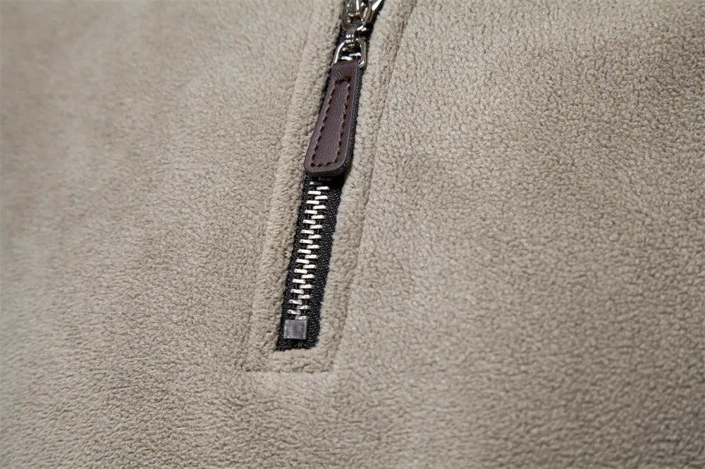Nahaufnahme eines beigen Fleece-Stoffes mit silbernem Reißverschluss und braunem Lederanhänger. Ideal für Mode, Textilien, Outdoor-Bekleidung.