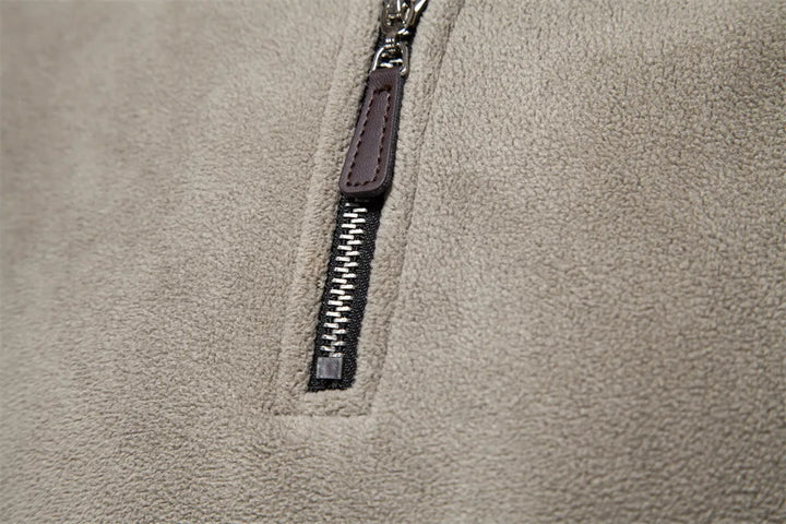 Nahaufnahme eines beigen Fleece-Stoffes mit silbernem Reißverschluss und braunem Lederanhänger. Ideal für Mode, Textilien, Outdoor-Bekleidung.