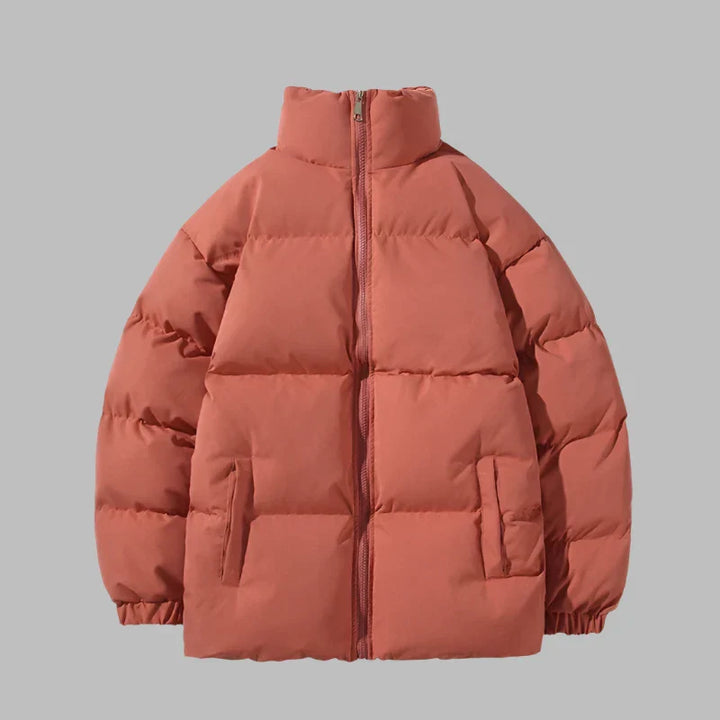 Orangefarbene Daunenjacke mit Reißverschluss, Stehkragen und Seitentaschen vor grauem Hintergrund. Wintermode, warme Oberbekleidung.