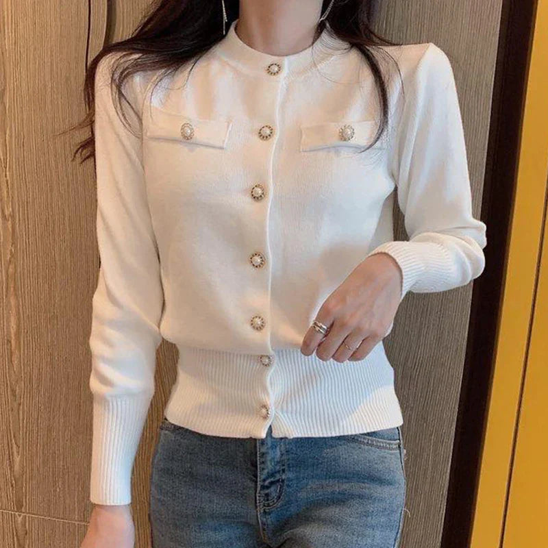 Frau trägt eleganten weißen Strick-Cardigan mit Perlenknöpfen, kombiniert mit blauer Jeans. Modischer Look, ideal für Herbstmode.