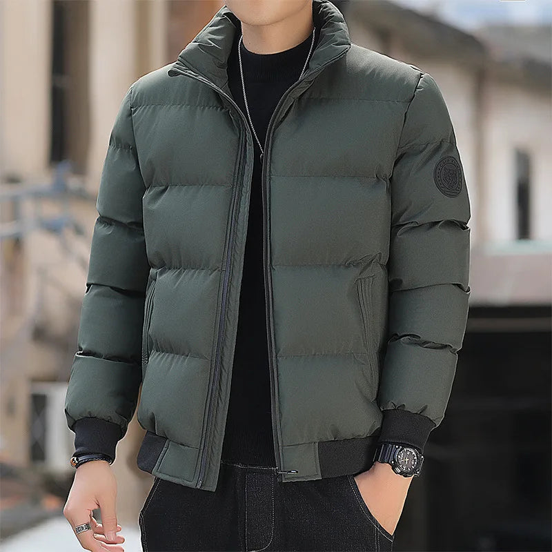 Mann in grüner Daunenjacke, schwarzem Pullover und Jeans. Modische Winterbekleidung, Outdoor-Stil, warme Jacke für kalte Tage.