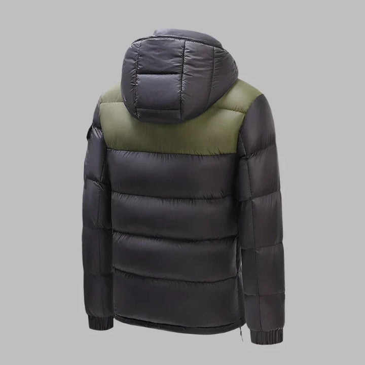 Schwarze Daunenjacke mit Kapuze, olivgrüner Schulterpartie, isoliert auf grauem Hintergrund. Wintermode, warme Outdoor-Bekleidung, Herrenjacke.