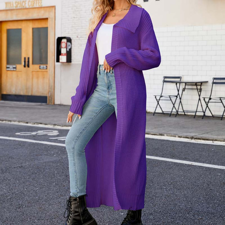 Frau in lila Strickmantel, weißem Top und blauer Jeans posiert auf Straße. Modetrend, Herbstmode, lässiger Stil, urbane Kulisse.
