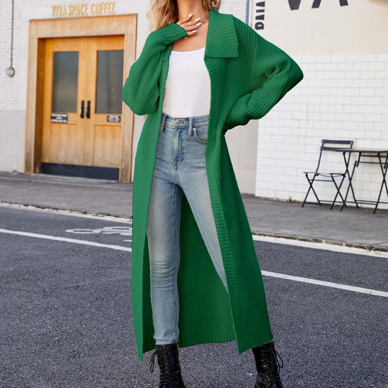 Frau in grünem Strickmantel, weißem Top und Jeans posiert auf Straße vor Café. Modetrend Herbst, lässiger Stil, urbane Mode.