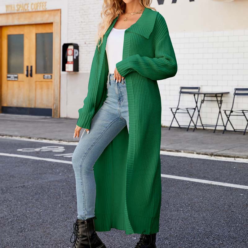 Frau in grünem Strick-Cardigan und Jeans posiert auf städtischer Straße vor Café. Modetrend Herbst, lässiger Stil, Streetwear.
