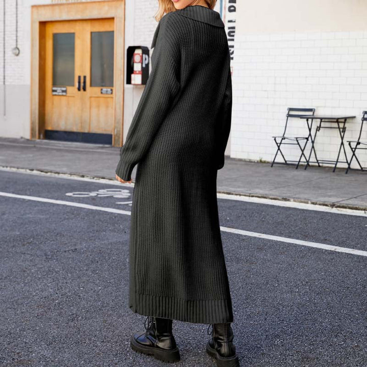 Frau in langem, schwarzem Strickkleid und Stiefeln steht auf städtischer Straße. Modetrend, Herbstmode, urbaner Stil, lässiges Outfit.