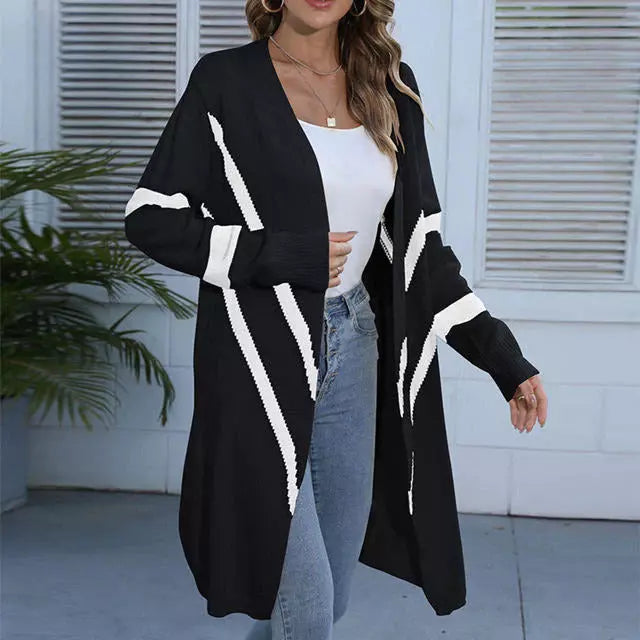 Frau in schwarzem Cardigan mit weißen Streifen, weißem Top und blauer Jeans vor Fenster. Modetrend, lässiger Stil, Damenmode.