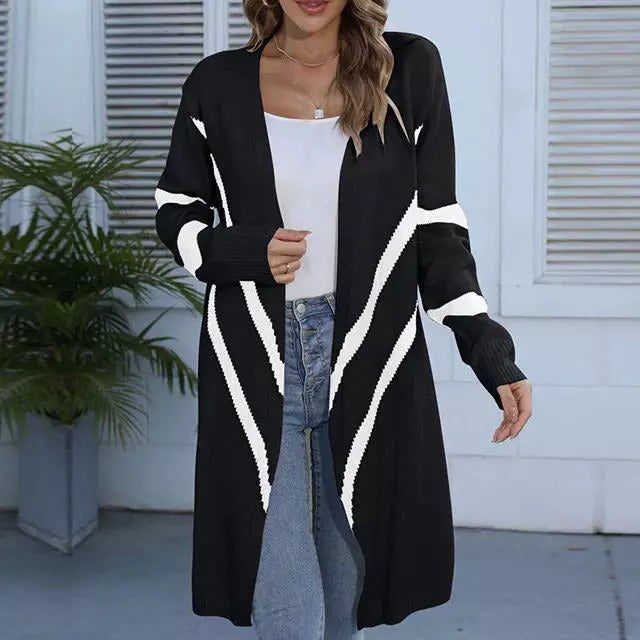 Frau trägt langen schwarzen Cardigan mit weißen Streifen, kombiniert mit weißem Top und blauer Jeans. Modetrend, Damenmode, Herbstoutfit.