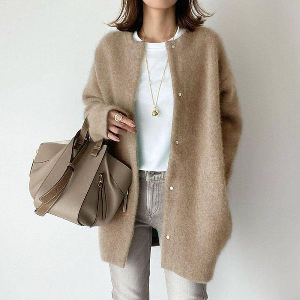 Frau in beigem Strickmantel, weißem T-Shirt und Jeans, hält eine beige Designer-Handtasche. Modetrend, Herbstmode, Damenbekleidung.