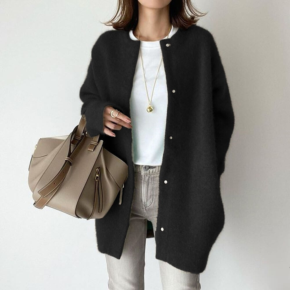 Dame in schwarzem Cardigan, weißem T-Shirt und grauer Hose, hält beige Handtasche. Modischer Herbst-Look, lässig und elegant.
