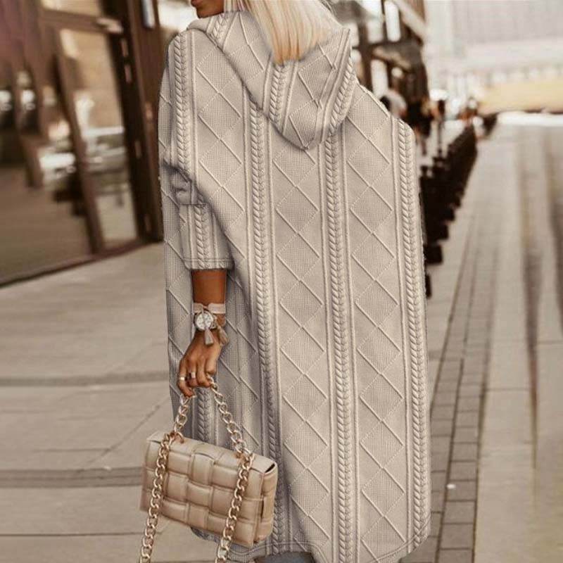 Frau in langem, grauem Strickmantel mit Kapuze, hält gesteppte Handtasche. Modischer Herbstlook auf städtischer Straße.
