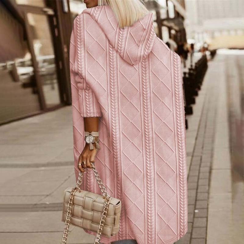 Frau in rosa Strickmantel mit Kapuze, hält eine gesteppte Handtasche, geht auf städtischem Gehweg. Modetrend, Herbstmode, Damenbekleidung.