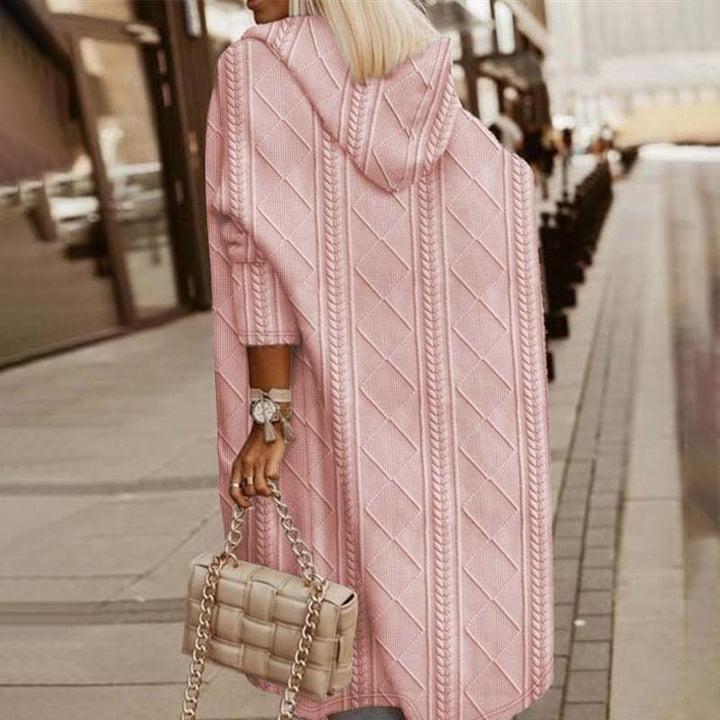 Frau in rosa Strickmantel mit Kapuze, hält eine gesteppte Handtasche, geht auf städtischem Gehweg. Modetrend, Herbstmode, Damenbekleidung.