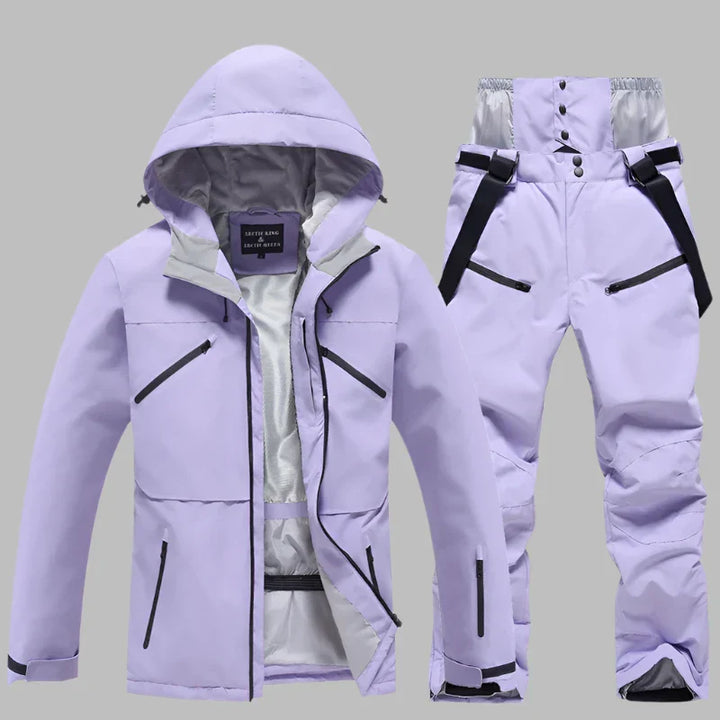 Lila Skianzug für Damen, bestehend aus wasserdichter Jacke mit Kapuze und passender Hose, ideal für Wintersport und Outdoor-Aktivitäten.