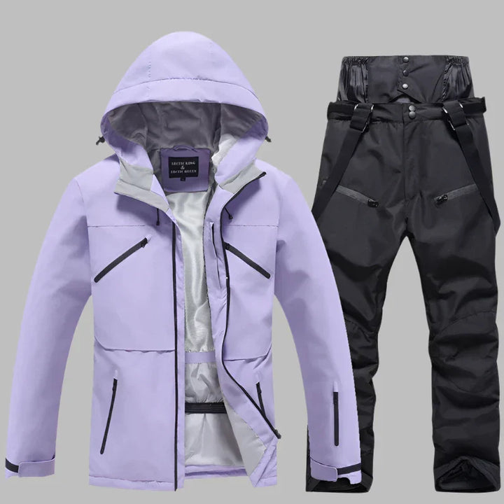 Lila Skijacke mit Kapuze und schwarze Skihose mit Hosenträgern auf grauem Hintergrund. Winterbekleidung, Outdoor, wasserdicht, atmungsaktiv.