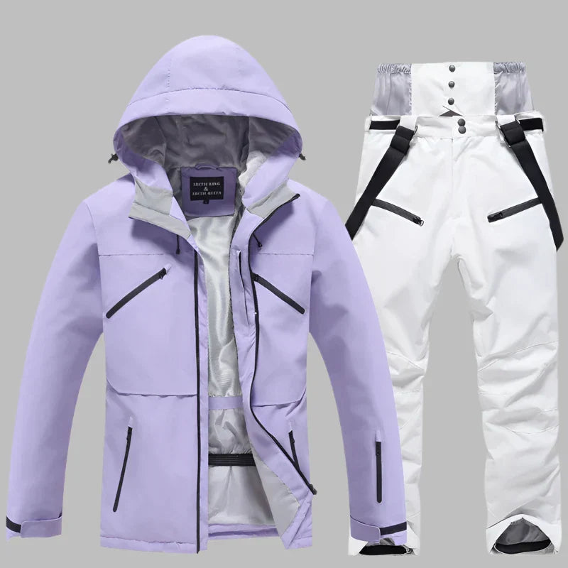 Lila Skijacke mit Kapuze und weiße Skihose mit Hosenträgern auf grauem Hintergrund. Winterbekleidung, Outdoor, wasserdicht, atmungsaktiv.