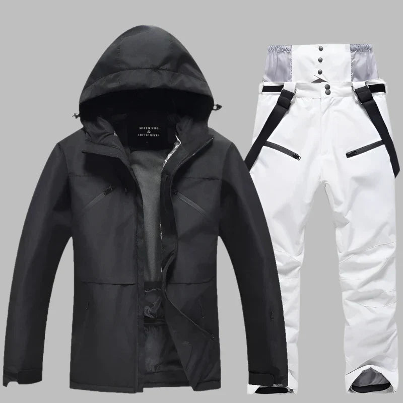 Schwarze Skijacke mit Kapuze und weiße Skihose mit Hosenträgern auf grauem Hintergrund. Winterbekleidung, Outdoor, wasserdicht, atmungsaktiv.
