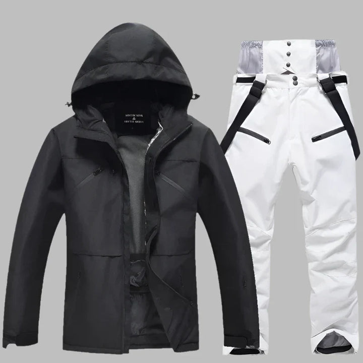 Schwarze Skijacke mit Kapuze und weiße Skihose mit Hosenträgern auf grauem Hintergrund. Winterbekleidung, Outdoor, wasserdicht, atmungsaktiv.