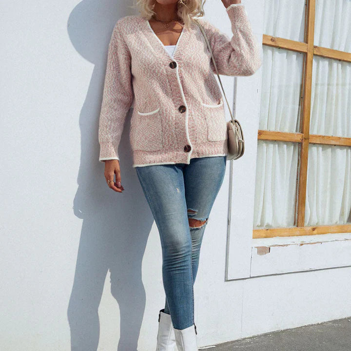 Frau in rosa Strickjacke, blauer Jeans und weißen Stiefeletten vor weißer Wand mit Fenster. Modetrend, lässiger Herbstlook, Damenmode.