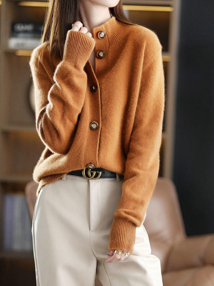 Frau trägt braunen Strickpullover mit Knöpfen, kombiniert mit weißer Hose und schwarzem Gürtel. Modetrend, Herbstmode, eleganter Look.