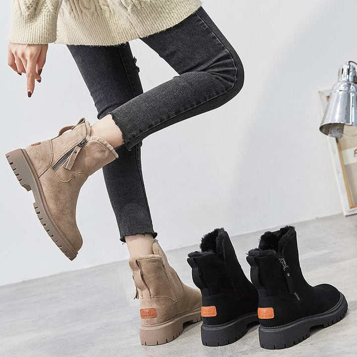 Frau trägt beige Stiefeletten mit Fransen, schwarze und beige Stiefel im Vordergrund. Modische Damenstiefel, Herbst-Winter-Trend, bequeme Schuhe.