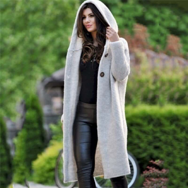 Frau in grauem Strickmantel mit Kapuze, schwarze Lederhose, draußen im Grünen. Modetrend, Herbstmode, stilvoller Look, Damenbekleidung.
